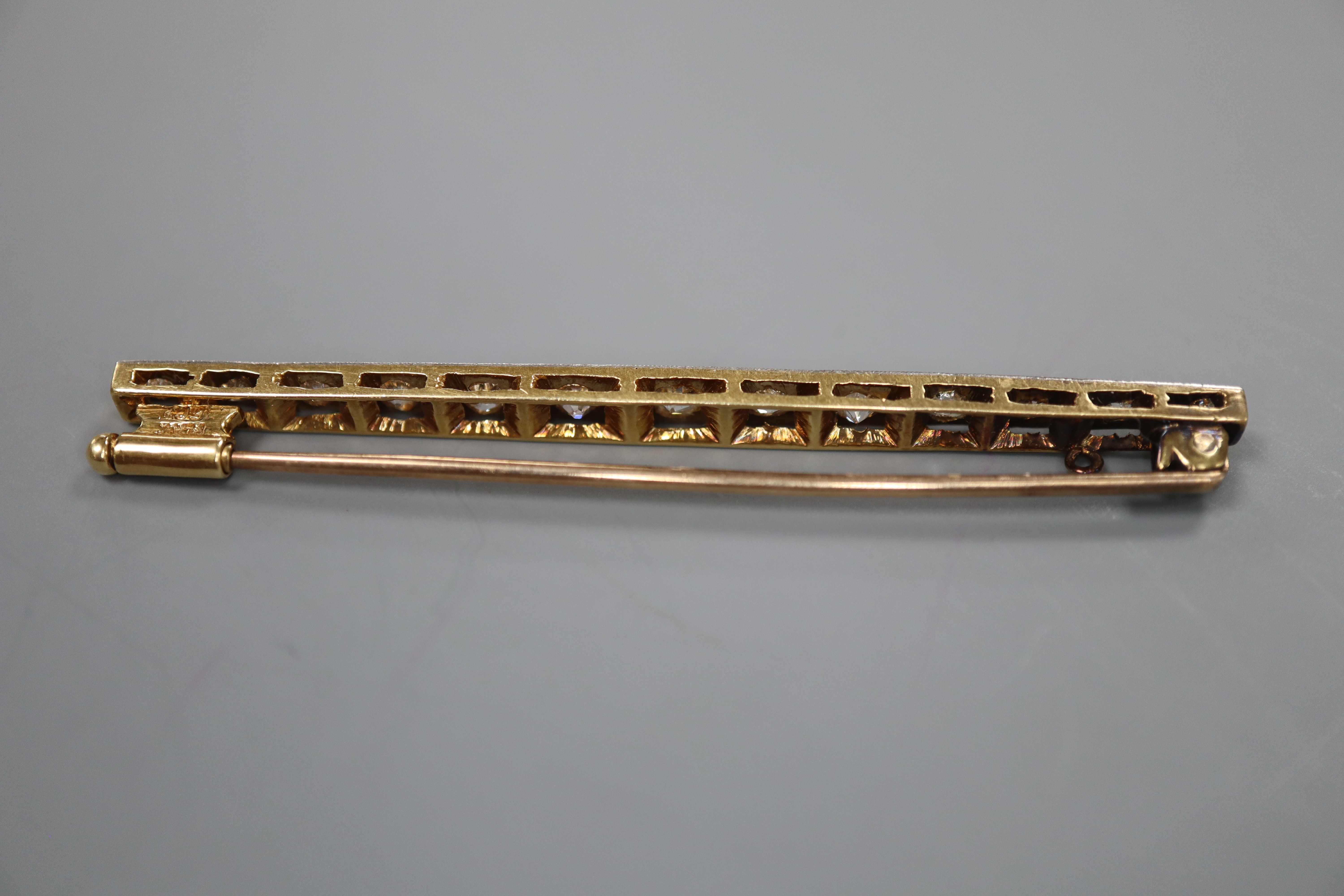 An early 20th century 15ct, plat and graduated thirteen stone diamond set bar brooch, 57mm, gross 4.7 grams.